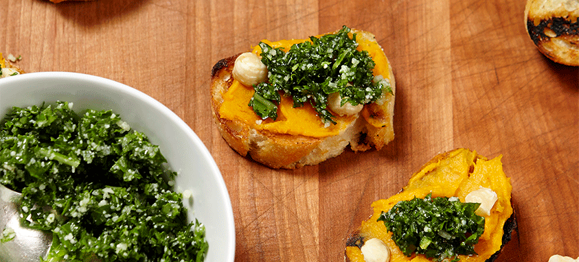 Kale, garlic, butternut squash crostini from Wolfgang Puck Catering. It sits on top of a wooden board