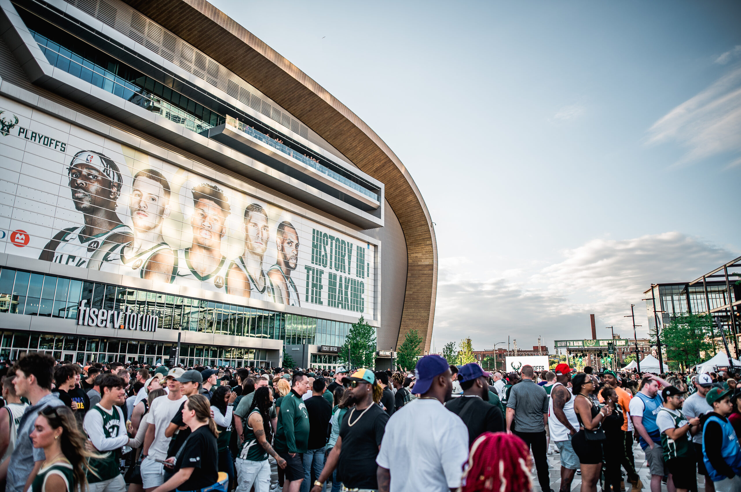 A crowd in front of the Old World Third Street Entertainment District. A banner is on the side of the building with five basketball players and text reading, "History in the making."