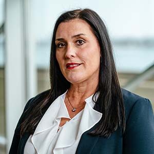 A portrait of Becky Bixby. She is a white woman with long black hair and a blue suit jacket