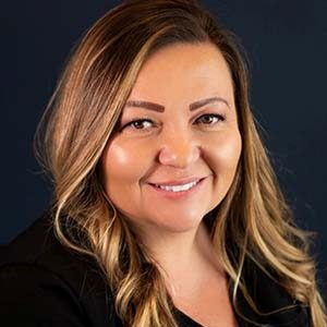 A portrait of Jaclyn Dawson. She is a brown woman with highlighted wavy hair and a black blouse