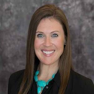 A portrait of Jennifer Toups. She is a white woman with long brown hair and a black collared shirt