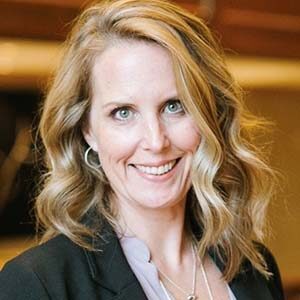 A portrait of Kristen Pryor. She is a blonde white woman with wavy hair and a grey suit jacket