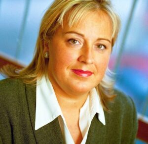 A portrait of Margaret Bowler. She is a blonde white woman with shoulder-length hair and a green cardigan