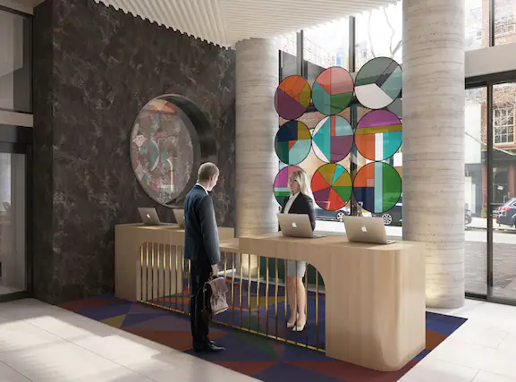 The reception desk of Motto by Hilton New York City Chelsea. Circular stained glass is behind the receptionist