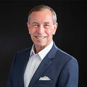 A portrait of Randy Zupanksi. He is an older white man with combed greying hair and a blue jacket