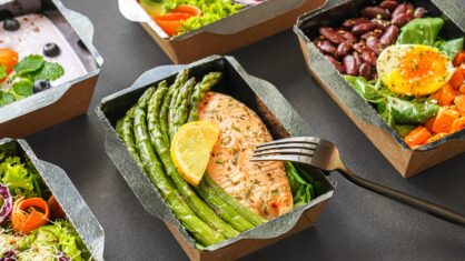 A small box of food with salmon, asparagus and a lemon wedge