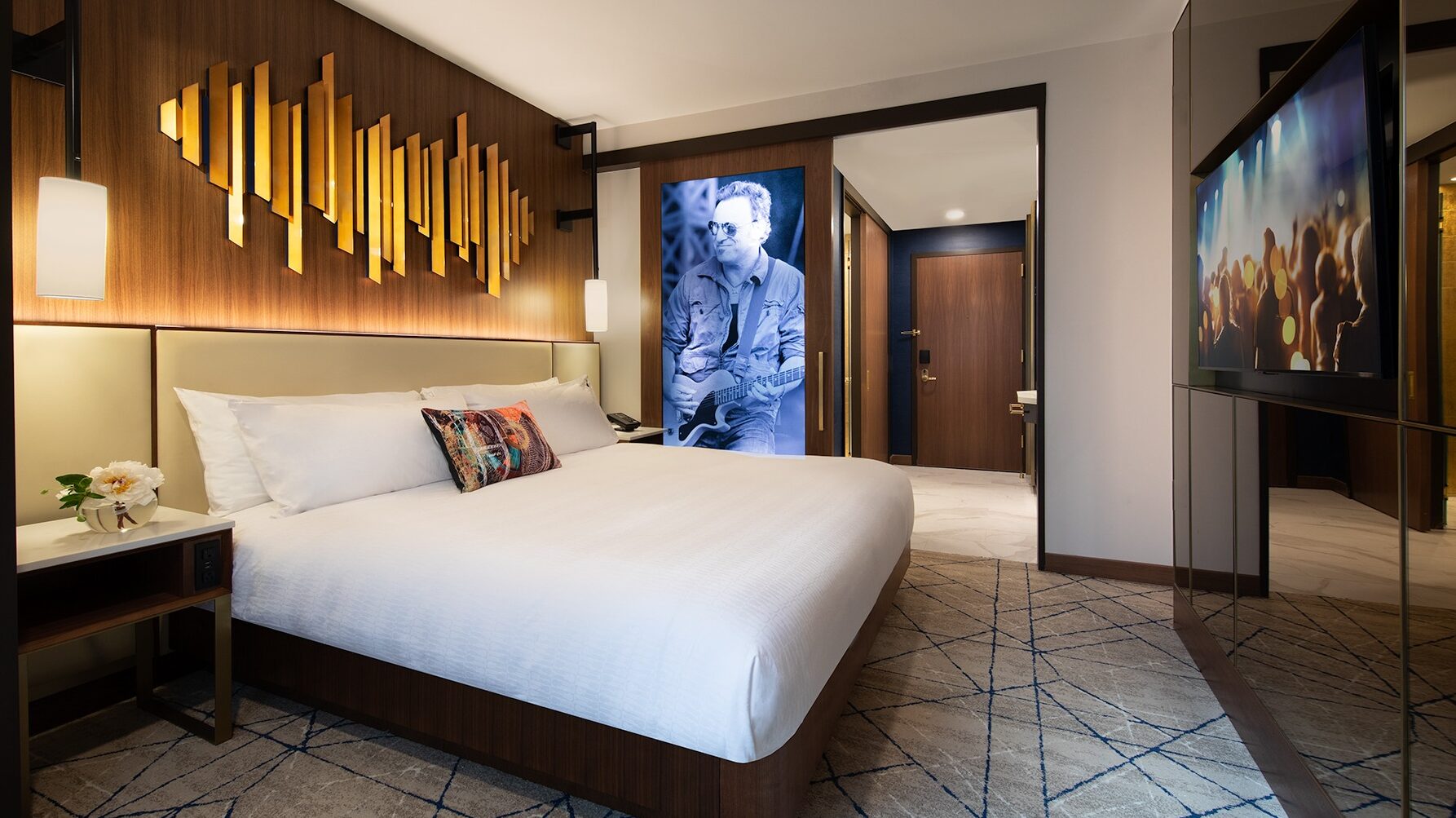 A guest room at hard rock hotel new york. There is a gold accent piece above the bed and a musician's portrait on the bathroom door