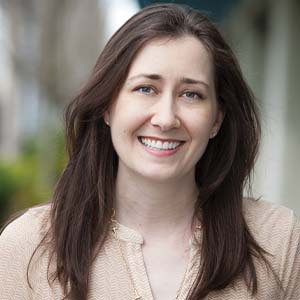 A portrait of Brooke Hall. She is a white woman with long dark hair and a blush blouse.