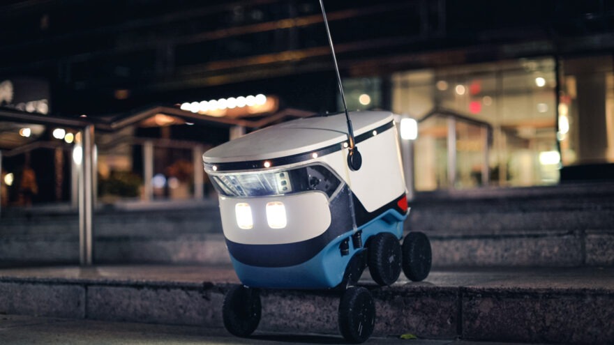 Cartken Robot. It is white and box-shaped with two lights and six wheels