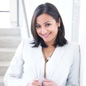 A portrait of Dee Patel. She is a brown woman with shoulder-length black hair and a white suit