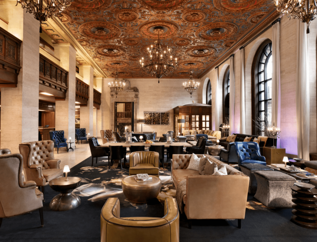 The lounge of Hotel Du Pont. Tan leather furniture is arranged in circles beneath an elaborate ceiling and chandeliers