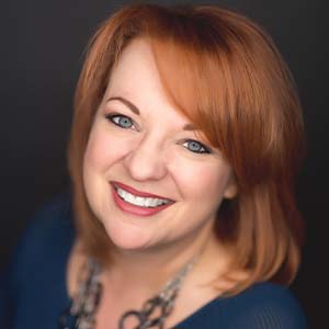 A portrait of Julie Stow. She is a white woman with straight red hair and a blue blouse