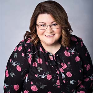 A portrait of LeAnna Toups-Bennett. She is a white woman with wavy brown hair and a black floral blouse