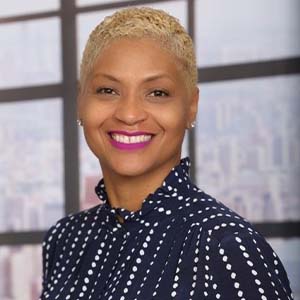 A portrait of Nicole Hankton. She is a black woman with buzzed blonde hair and a black polka-dot blouse