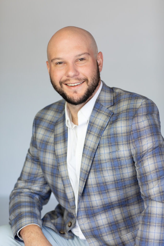 A portrait of Robert Bronstein. He is a bald white man with a short black beard and grey plaid suit jacket