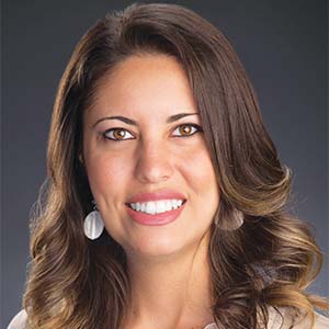 A portrait of Sasha Lee. She is a white woman with wavy brown hair and white earrings