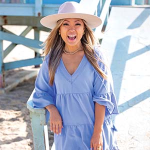 A portrait of Thuy Diep. She is a Vietnamese woman with a blue sundress and white hat