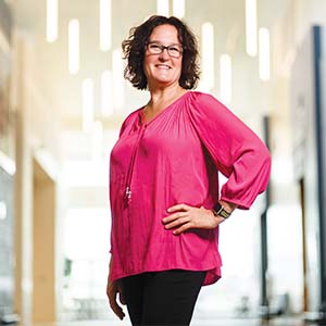 A portrait of Tracy Stuckrath. She is a white woman with short curly hair and a pink blouse