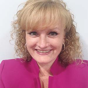 A portrait of Yvette Campbell. She is a blonde white woman with a perm and a bright pink jacket