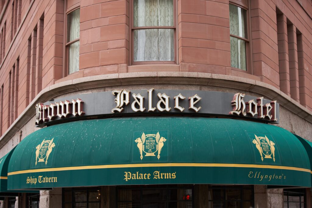 An awning at The Brown Palace Hotel and Spa, Autograph Collection. It is green with the hotel's emblem and the names of hotel restaurants