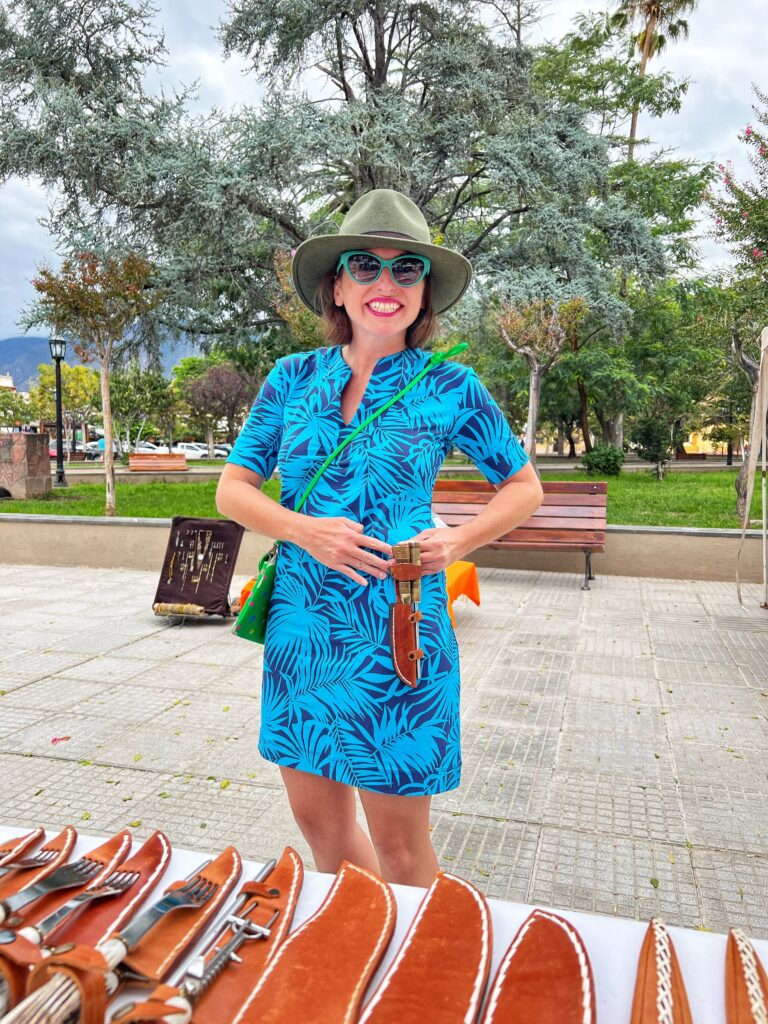 Ashley Lawson holding a knife and cutlery set with a leather sheath at an artisanal market