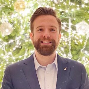 A portrait of Keith Cestare. He is a white man with combed red hair, a red beard and a grey suit