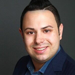 A portrait of Mark Catuogno. He is a brown man with combed black hair and a blue suit