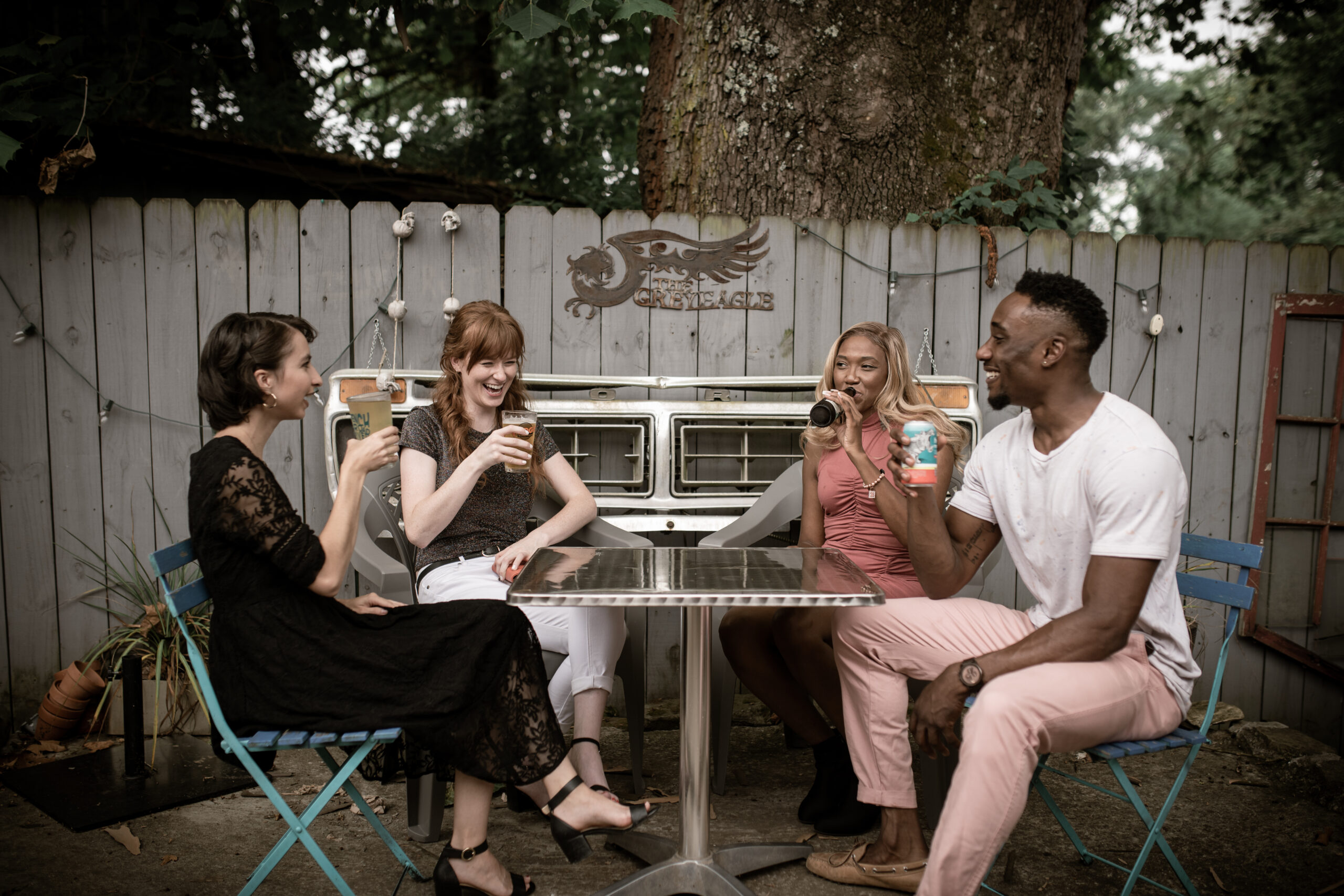 A group of four young adults drinking at an rustic outdoor table.