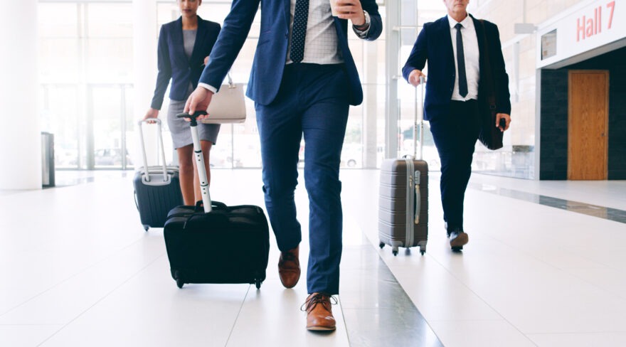 Several business people walking through an airport with small suitcases
