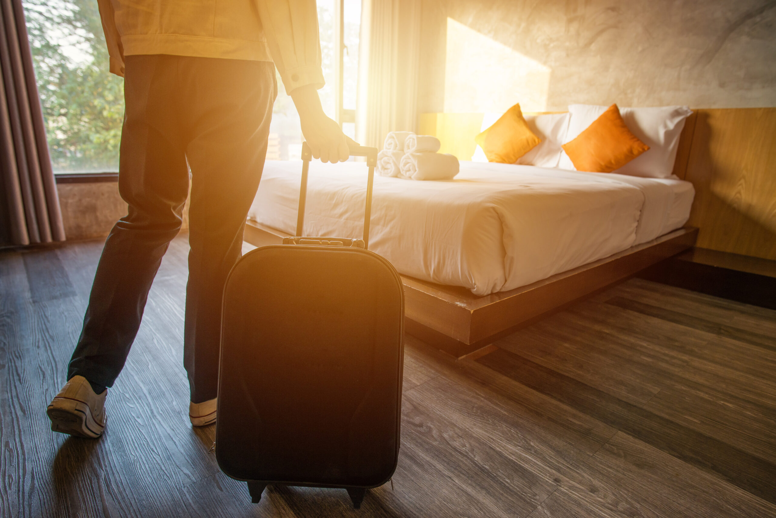 A traveler holding a roller suitcase in a hotel room.