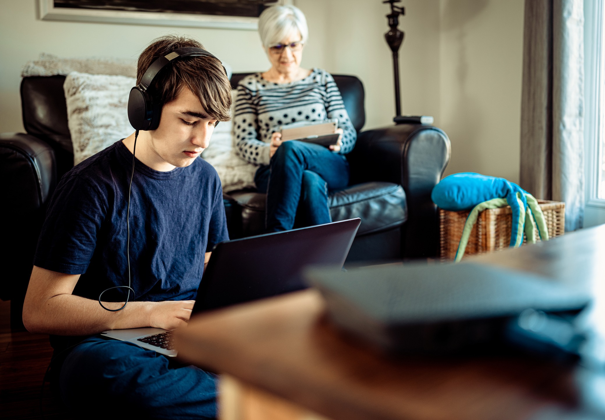 A teenager with headphones plugged into his laptop and an older woman using a tablet