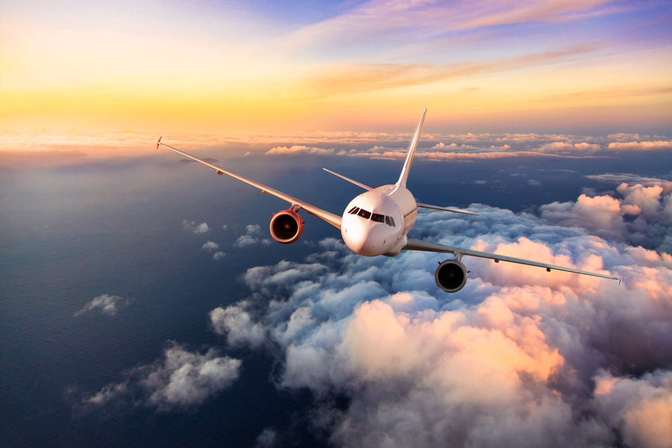 An unbranded airplane flying above the ocean at sunset