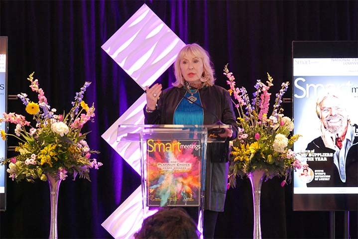 Marin Bright speaking at the Louisville Smart Meetings experience. Two large bouquets of flowers are on either side of her