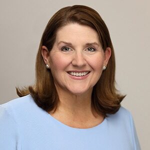 A portrait of Michelle McKinney Frymire. She is a white woman with shoulder-length brown hair and a blue blouse.