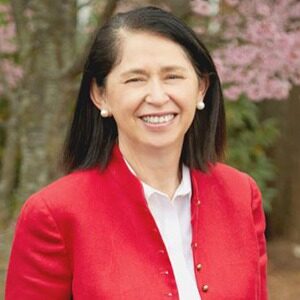 A portrait of Amanda Hawkins-Vogel. She is an older woman with shoulder-length black hair and a red cardigan.