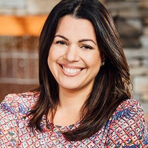 A portrait of Laura Maldonado. She is a light-skinned woman with straight black hair and a red patterned blouse.