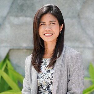 A portrait of Nattinee McMillan. She is a Thai woman with long dark hair and a grey cardigan.