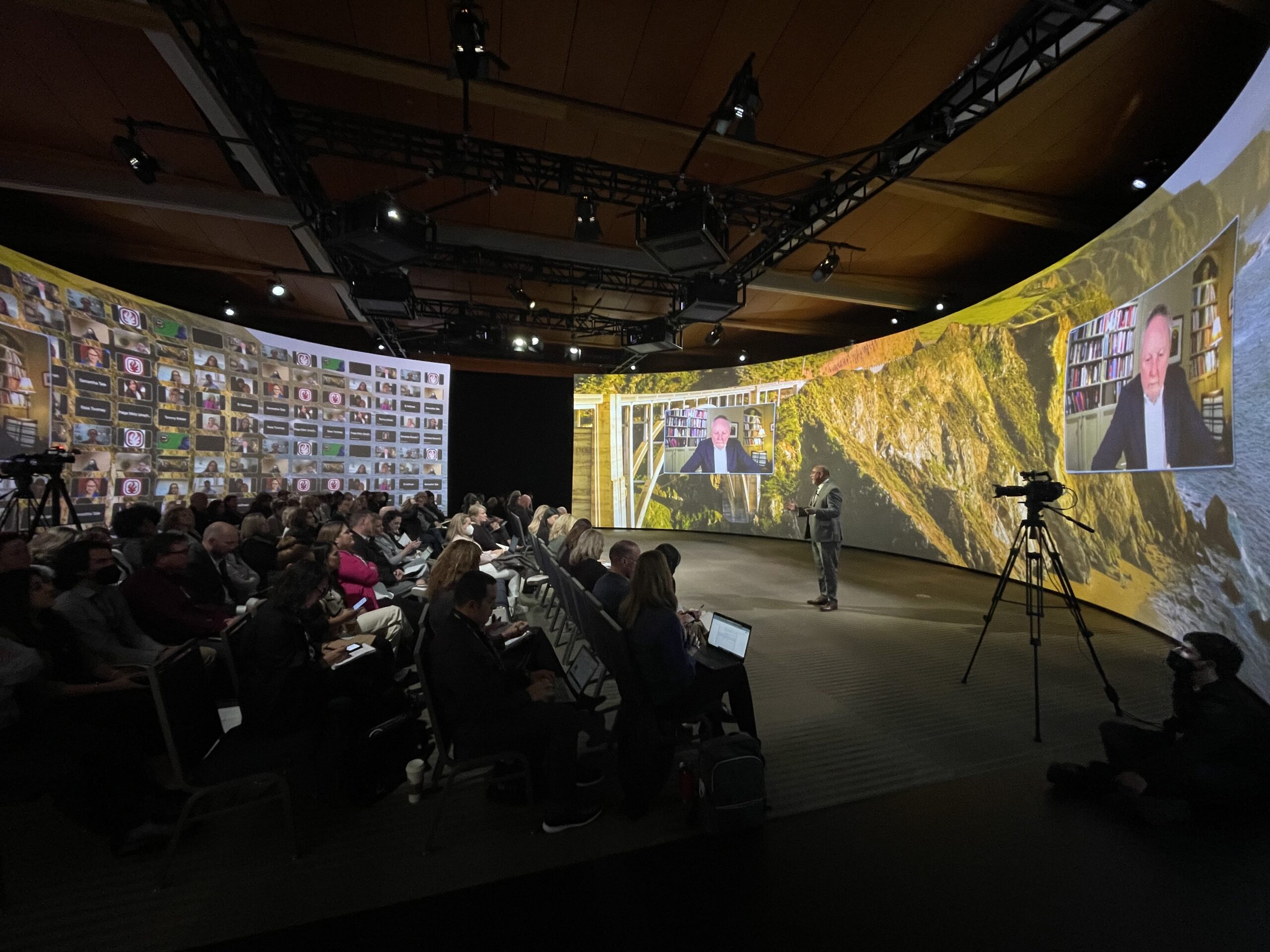 A speaker gives an address to a small crowd in the Immersive Design Studios' CANVAS Studio at Monterey Conference Center in California. Projector screens wrap around the round room.
