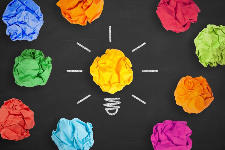 A black background with colored balls of paper. One forms a lightbulb, representing new business ideas.