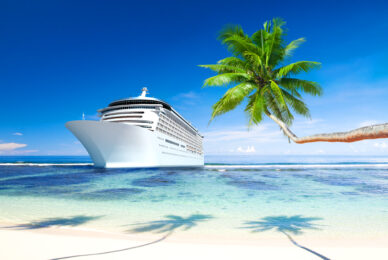 A cruise line ship sails past a beach and palm tree
