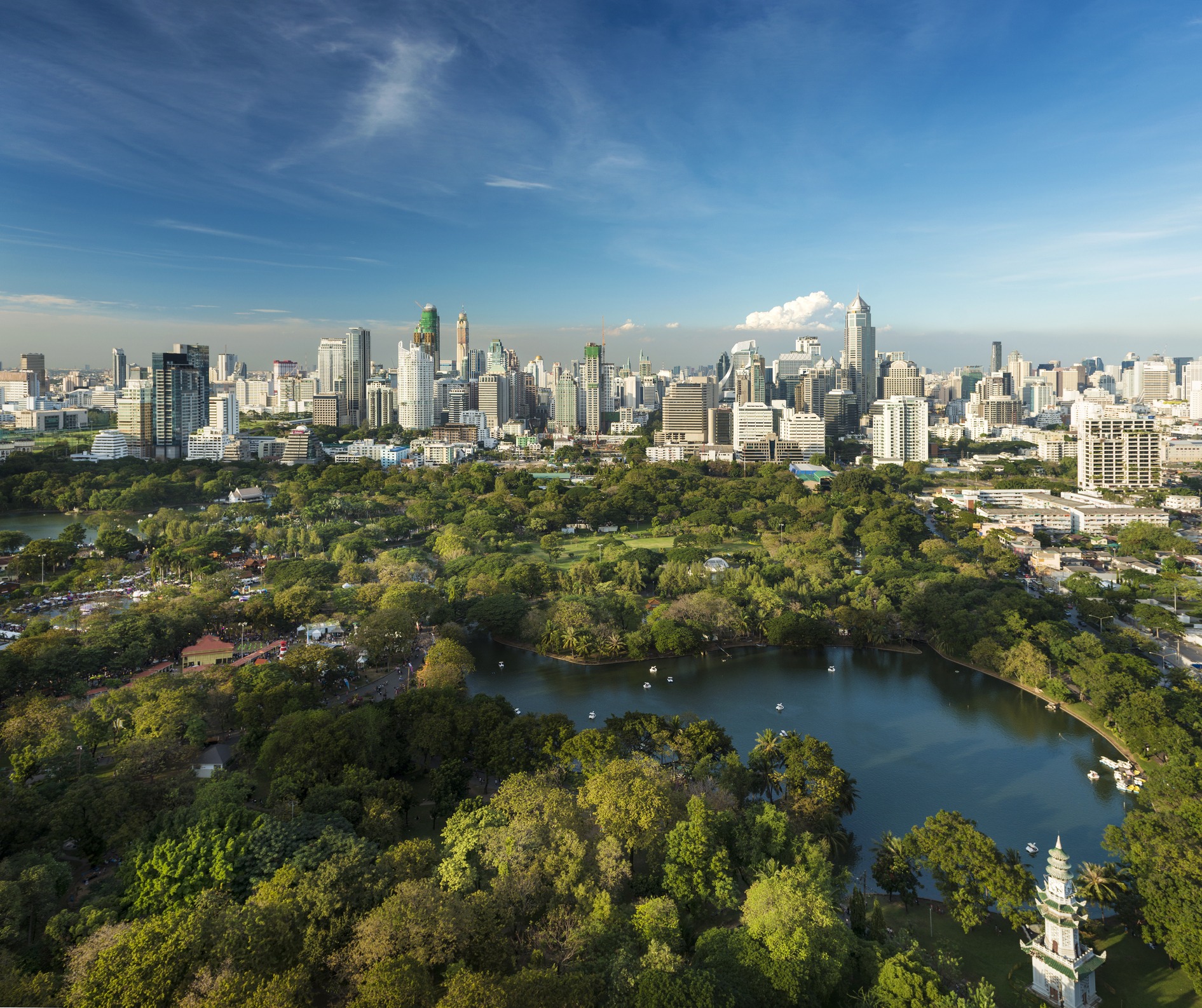 An aerial shot of the Bangkok skyline. The city sits behind a forest and lake.