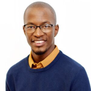 A portrait of Sinothando Adonisi, a young bald black man with a yellow collared shirt under a blue sweater.