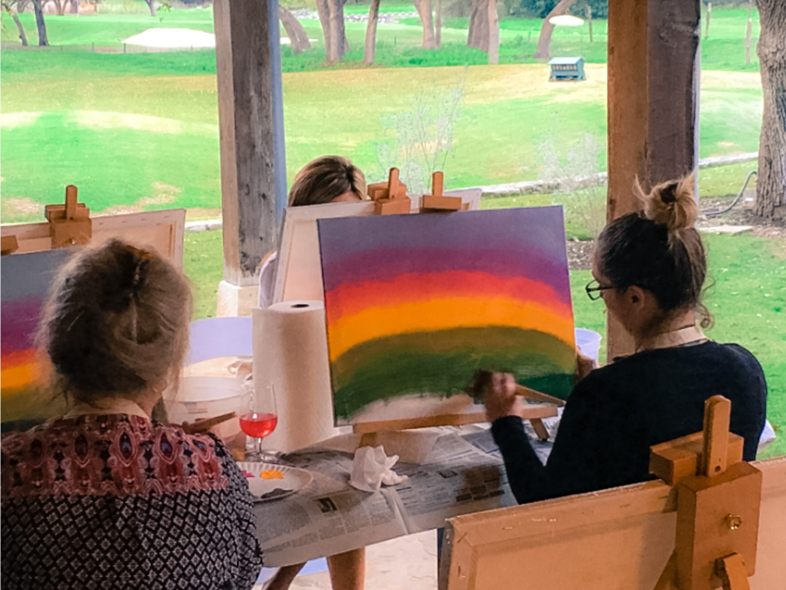 Women painting abstract sunsets on a lawn.