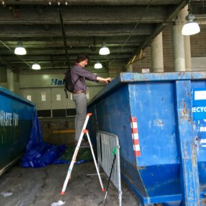 MeetGreen Director of Sustainability Eric Wallinger stands on a ladder and looks over the side of a dumpster.