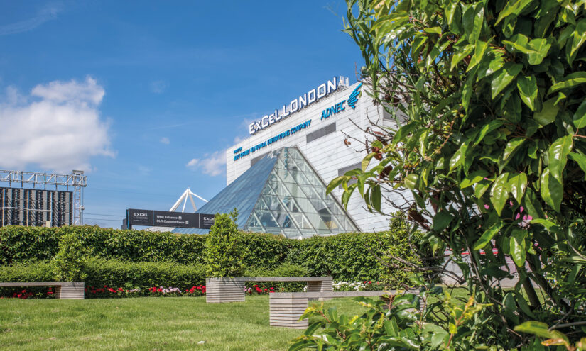 An exterior shot of ExCel London's event center. It sits behind a lawn and series of hedges.