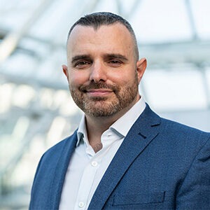 A portrait of Jamie Ades. He is a man with a short beard and a blue suit.