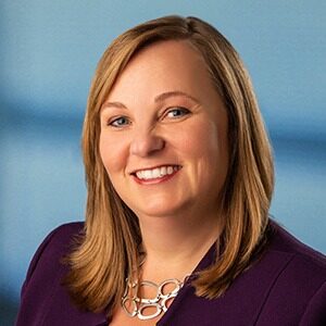 A portrait of Kristen McGrath. She is a white woman with light brown hair and a dark purple blouse.