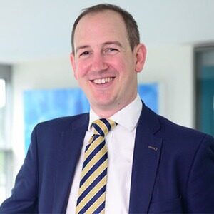 A portrait of Matt Gleaves. He is a balding white man with a blue suit and striped tie.