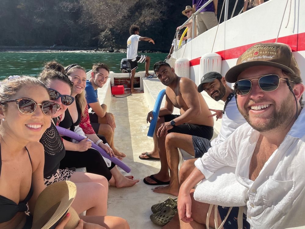 A group of coworkers on a teambuilding excursion. They are on a boat together wearing swimsuits and sunglasses.
