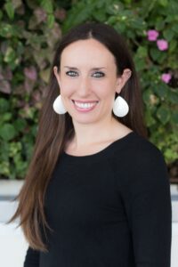 A portrait of Melissa Woodley, the author of this article. She is a white woman with long brown hair, large white earrings and a black blouse.